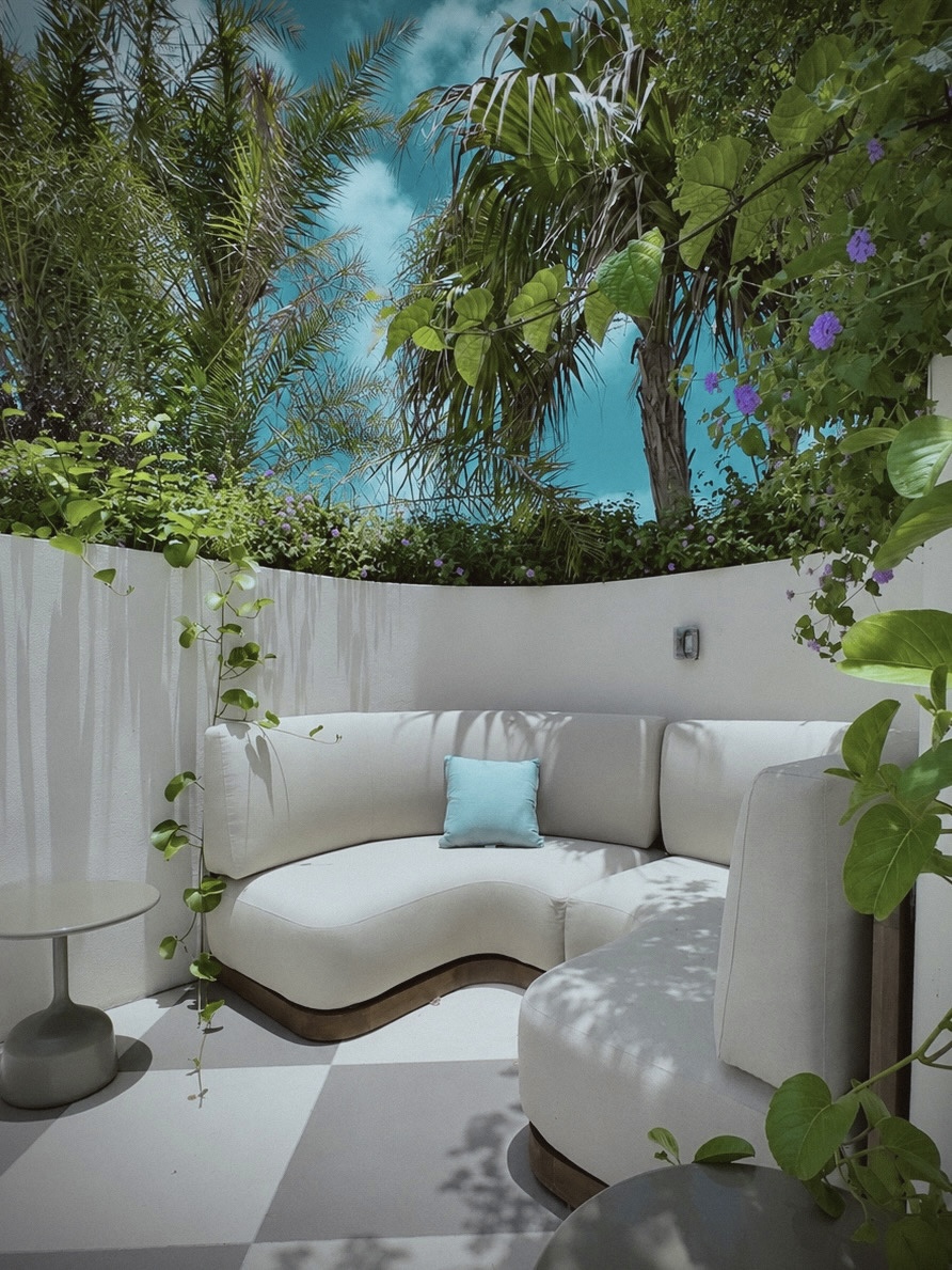 Private courtyard nook with curved white sofa under palms and bougainvillea