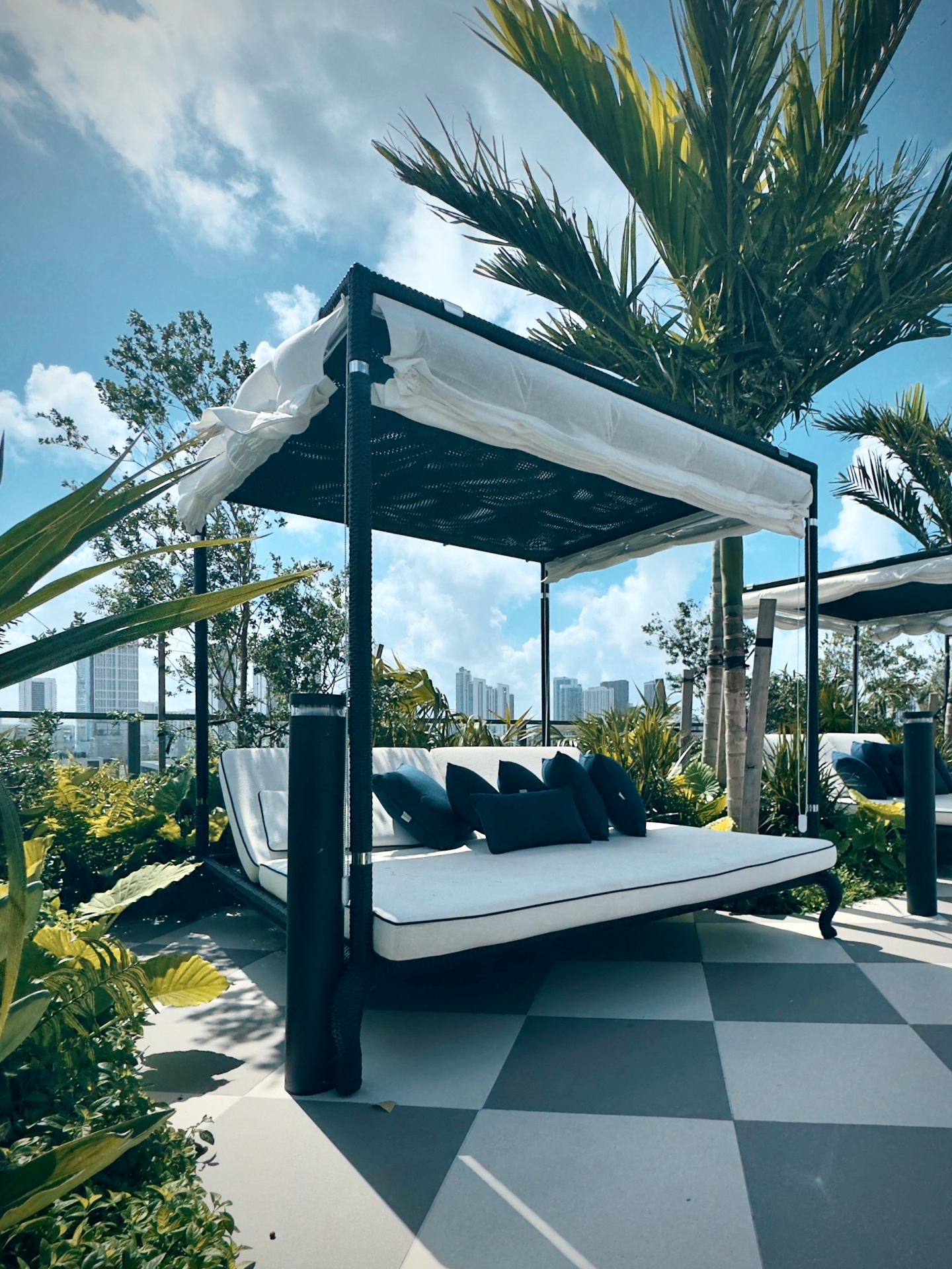 Canopied rooftop daybed surrounded by tropical plants with city views