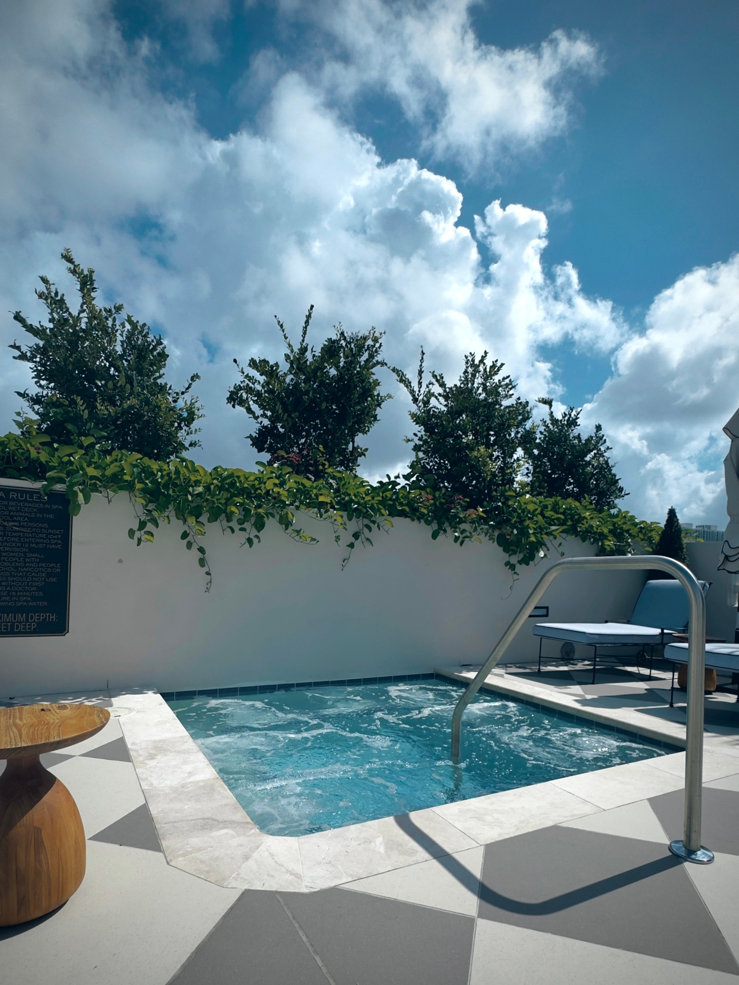 Rooftop hot tub on checkered tile with lush greenery and open sky