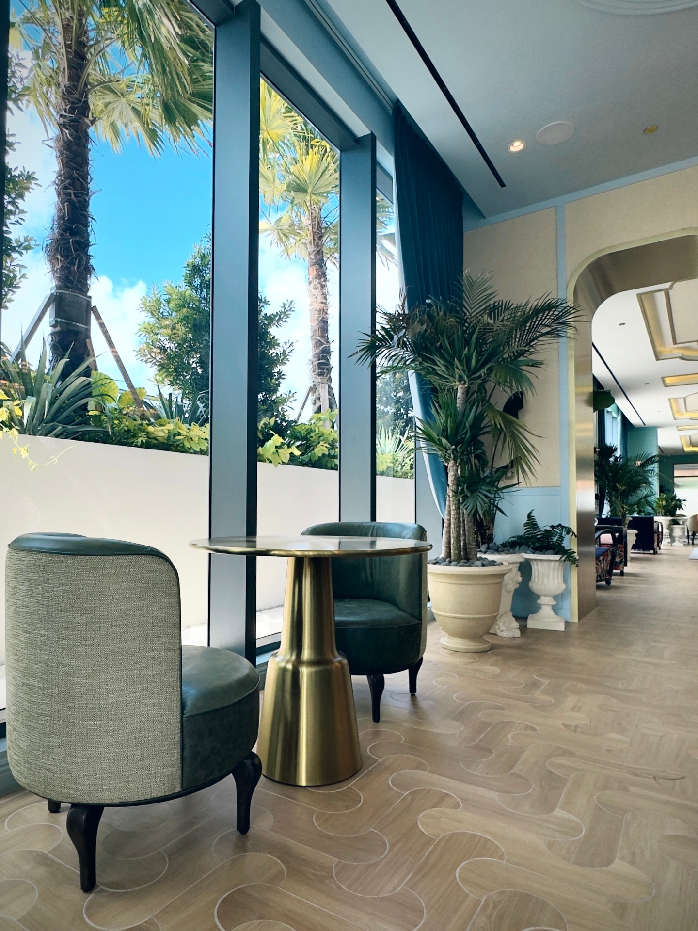 NoMad Wynwood lobby with velvet chairs, brass table, and floor-to-ceiling palm views