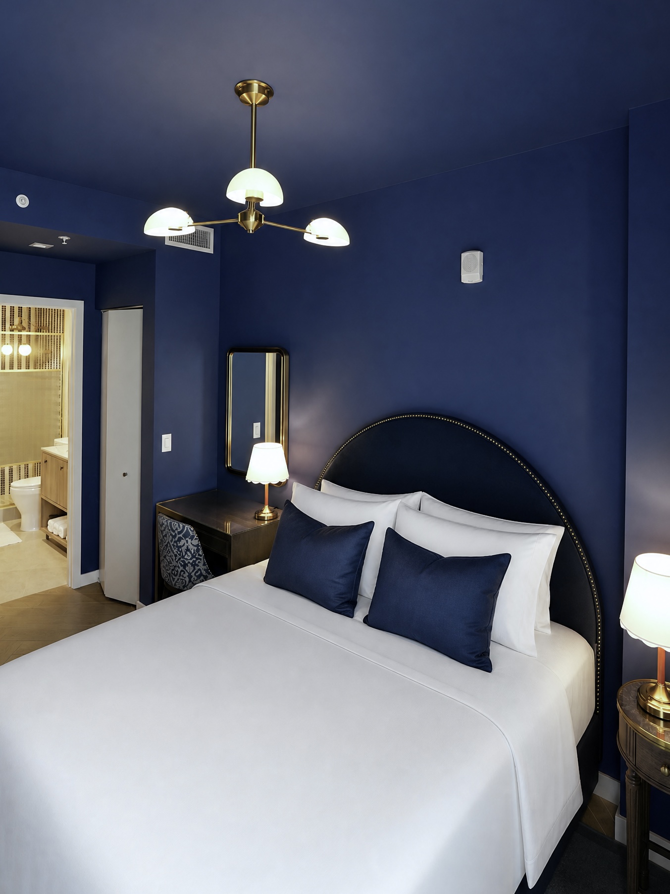 Deep blue bedroom with arched headboard and brass chandelier