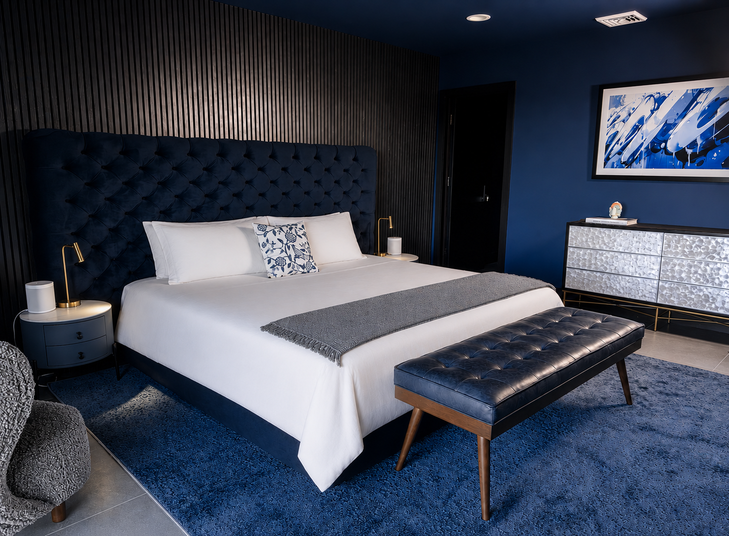 Deep blue bedroom with tufted velvet headboard and contemporary art